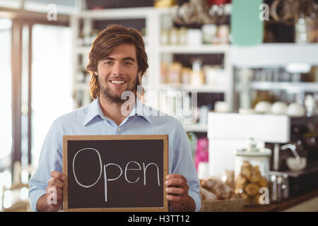 Portrait of waiter showing chalkboard with open sign Banque D'Images