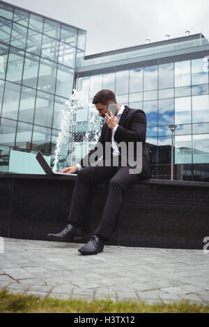 Businessman using laptop while talking on phone Banque D'Images