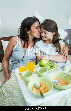 Mère Fille, baiser sur les joues en prenant votre petit-déjeuner sur le lit Banque D'Images