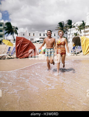 Années 1950 Années 1960 HAPPY COUPLE LOOKING AT CAMERA RUNNING ON TROPICAL BEACH FLORIDE USA Banque D'Images