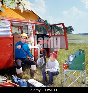 1970 MAN AND BOY CAMPING FILS assis par un réchaud portatif PÈRE ASSIS PAR CAMPING-avec des cannes à pêche et des engins Banque D'Images