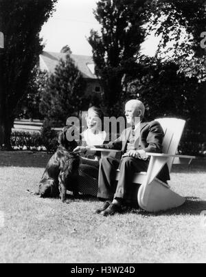 1930 Un homme âgé ASSIS SUR CHAISE ADIRONDACK DANS LA COUR Jeune femme agenouillée à côté de lui avec chien Setter Irlandais Banque D'Images