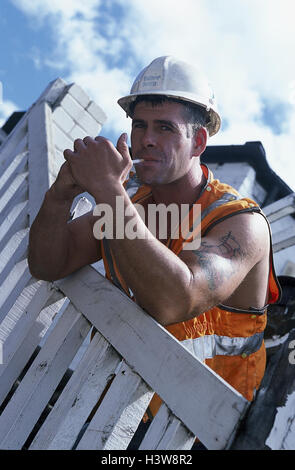 Clôture, travailleur de la construction, maigre, cigarette, lumière, modèle sorti, très près, garde-corps, clôture en bois, l'homme, travailleur, fumeur, fumeur d'une pause, pause de travail, casque de sécurité, casque, casque, harnais, tatouage, partie supérieure du bras, de la fumée, nuisibles, mania, risque pour la santé Banque D'Images