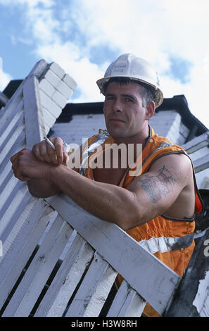 Clôture, travailleur de la construction, maigre, la cigarette, la permission du modèle, très près, garde-corps, clôture en bois, l'homme, travailleur, fumeur, fumeur d'une pause, pause de travail, d'expression, casque, casque de sécurité, casque, harnais, tatouage, haut du bras Banque D'Images