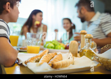 Garçon assis à table à manger avec un plateau de pain français à l'avant Banque D'Images