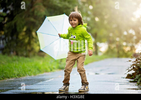 Adorable petit garçon avec parapluie dans un parc un jour de pluie, jouant et sautant, smiling, temps d'automne Banque D'Images