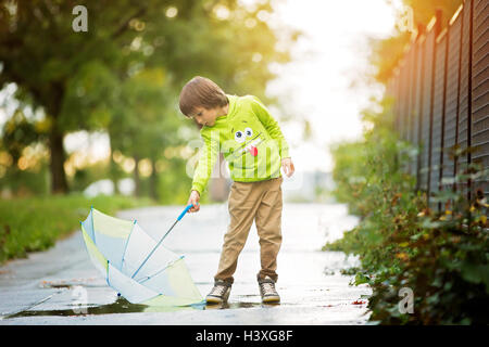 Adorable petit garçon avec parapluie dans un parc un jour de pluie, jouant et sautant, smiling, temps d'automne Banque D'Images