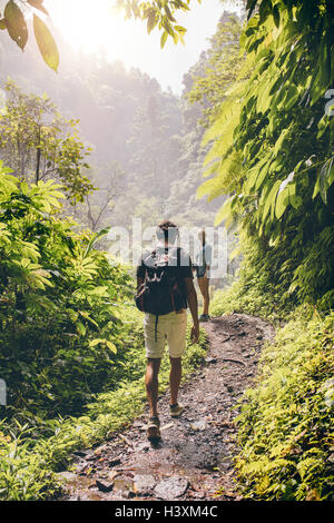 Vue arrière coup de jeune couple en train de marcher le long d'un chemin dans l'arbre. L'homme et la femme la randonnée sur sentier forestier. Banque D'Images