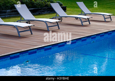 Des chaises longues sur la terrasse en bois à côté d'une piscine extérieure Banque D'Images