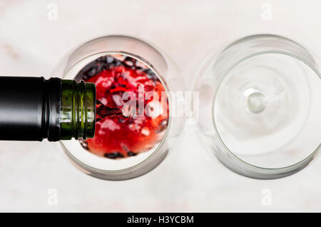 Verseur à vin rouge de la bouteille en verre. Deux verres sur la table de marbre blanc. Banque D'Images