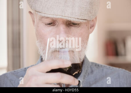 Vieil homme à cap holding wineglass. L'odeur du vin rouge avec sérieux. Banque D'Images