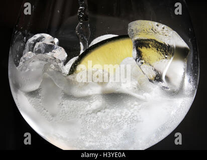 Un gin tonic est versé dans un bar avec une tranche de citron vert et de glace. Banque D'Images