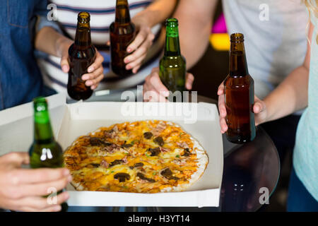 Groupe d'amis ayant une bouteille de bière et de pizza en partie Banque D'Images