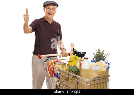 Cheerful senior posant avec un panier plein de provisions et de donner un pouce vers le haut isolé sur fond blanc