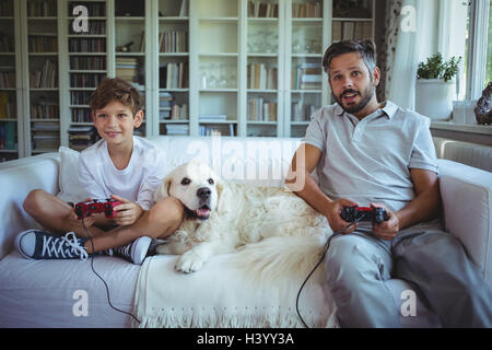 Père et fils assis sur le canapé avec le chien et à jouer aux jeux vidéo Banque D'Images