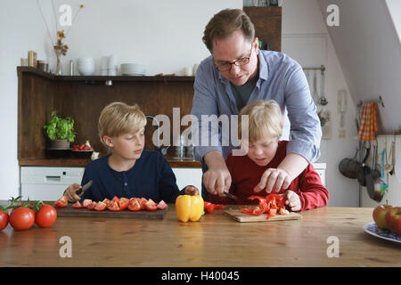Père fils handicapé aider à couper les légumes avec boy at table in kitchen Banque D'Images