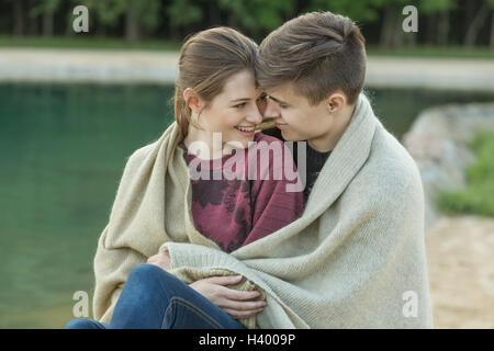 Smiling young couple aimant enveloppé dans le contrat cadre reposant au bord du lac Banque D'Images