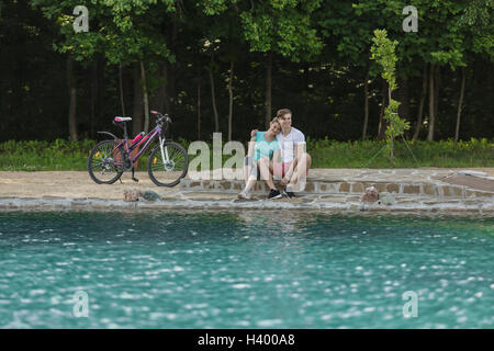 Smiling couple sitting by lake in park Banque D'Images