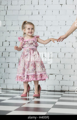 Happy girl in pink dress wearing oversized High heels standing at home Banque D'Images