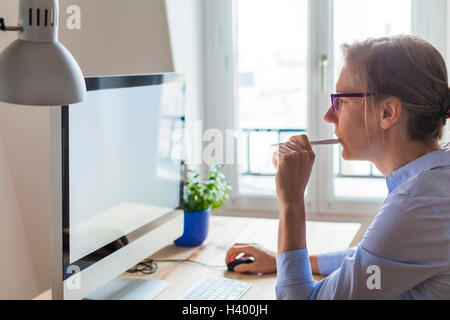 Jeune femme d'affaires de la pensée dans le projet avant de l'ordinateur à l'intérieur de bureau moderne Banque D'Images