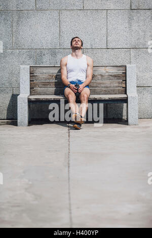 Assez jeune homme assis sur le banc en bois contre le mur Banque D'Images