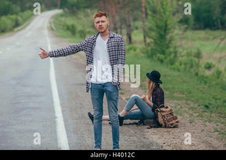 Alors que l'auto-stop homme femme assise sur la route Banque D'Images