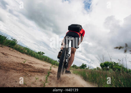 Low angle view of man Riding Mountain vélo sur route de terre contre ciel nuageux Banque D'Images