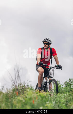 Homme confiant équitation vtt contre ciel nuageux Banque D'Images