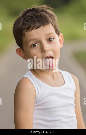 Portrait of boy sticking out tongue while standing at park Banque D'Images