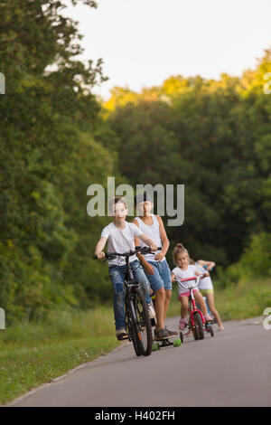 Frères et sœurs à vélo sur route contre des arbres au parc Banque D'Images