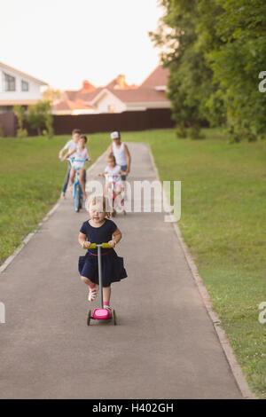 Vélo fille avec les frères et sœurs sur la route au milieu de Grassy field at park Banque D'Images