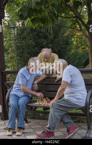 Senior friends jouer aux échecs sur banc de parc contre des arbres Banque D'Images