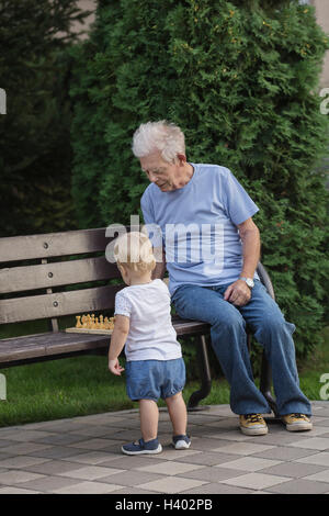 Grand-père jouer aux échecs avec fille sur le banc de parc contre l'arbre Banque D'Images