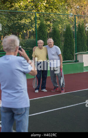 Vue arrière du man photographing friends standing contre clôture à court de tennis Banque D'Images