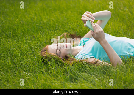 Young woman using phone while lying on grassy field Banque D'Images