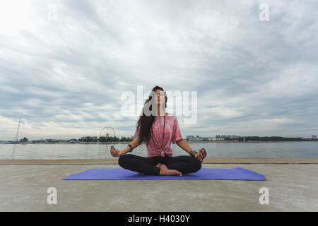 Woman meditating in lotus position à berge contre ciel nuageux Banque D'Images