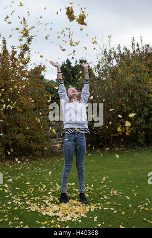 Jeune fille jetant une pile de feuilles dans l'air pour célébrer l'automne Banque D'Images