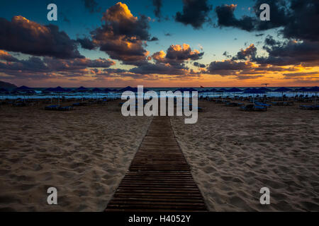 Passerelle en bois entre parasols et chaises longues sur la plage au coucher du soleil, plage de Georgioupolis, Crète, Grèce Banque D'Images