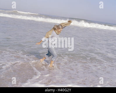 Plage de sable, mer, senior, heureux, de l'eau peu profond, courir, profiter vue latérale, femme, meilleur âge, 60-70 ans, poil long, à poil gris, prêt-à-porter, jeans, chiffon, Stola, loisirs, mode de vie, de repos, loisirs, vacances, plaisir, bonne humeur, gaieté, exubera Banque D'Images