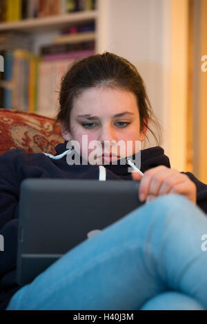 Young woman relaxing, assis sur un canapé à la maison, regardant vers le bas dans un Apple iPad - il est absorbé, une fixation sur la tablette. Banque D'Images