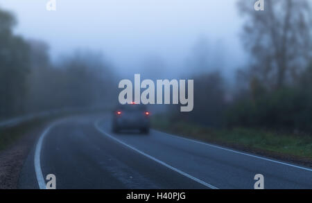 Voiture avec feux rouge va sur une route de campagne vide en automne sombre matin brumeux, correction tonale bleu effet de filtre. D peu profondes Banque D'Images