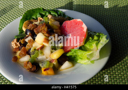 Assiette de dés de fruits mélangés sur lit de légumes verts Banque D'Images