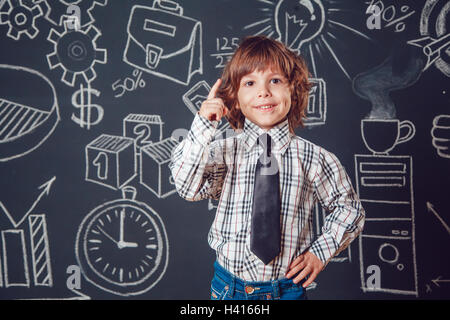 Petit garçon comme businessman ou enseignant de porter chemise et cravate de soulever un doigt vers le haut sur fond sombre avec business school photo Banque D'Images