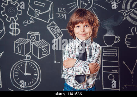 Petit garçon comme businessman ou enseignant de porter chemise et cravate. Debout les mains jointes sur fond sombre avec business school photo Banque D'Images