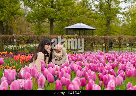 Deux jeunes femmes assis parmi des tulipes à Keukenhof jardin et avoir leurs photographies prises, Lisse, Hollande, Pays-Bas. Banque D'Images