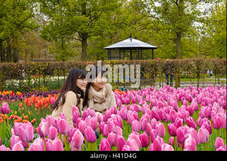 Deux jeunes femmes assis parmi des tulipes à Keukenhof jardin et avoir leurs photographies prises, Lisse, Hollande, Pays-Bas. Banque D'Images