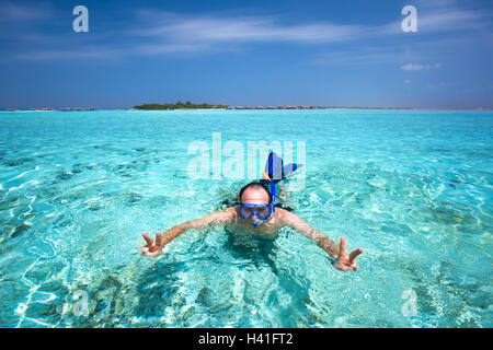 Jeune homme snorkling en lagune tropicale avec des bungalows sur pilotis Banque D'Images