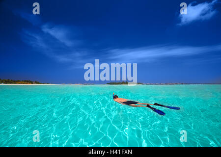 Jeune homme snorkling en lagune tropicale avec des bungalows sur pilotis Banque D'Images