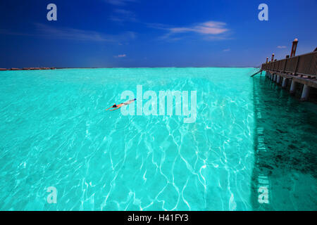 Jeune homme snorkling en lagune tropicale avec des bungalows sur pilotis Banque D'Images