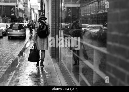 Homme marchant avec shopping jusqu'Berwick Street à Soho, à Londres, avec la réflexion dans le miroir. Banque D'Images